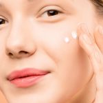 una mano aplicando crema sobre las mejillas de la cara
